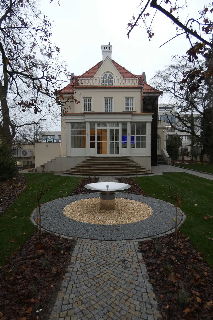 Prvorepubliková vila s nově dokončeným rondelovým parterem, dlážděnou osou a kruhovou fontánou uprostřed.