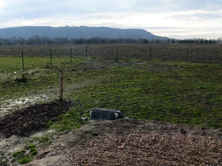 Před realizací Nepěkná, prázdná, zatravněná plocha oddělená plotem od pole.