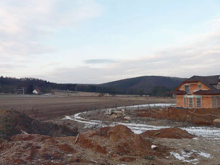 Před realizací Pole s hromadami hlíny a rozestavěným domem.