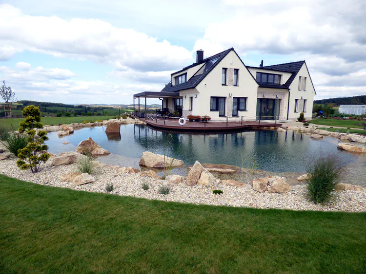 Po realizaci Průzračné jezero s molem amělkou zónou s vodními rostlinami u moderní novostavby.