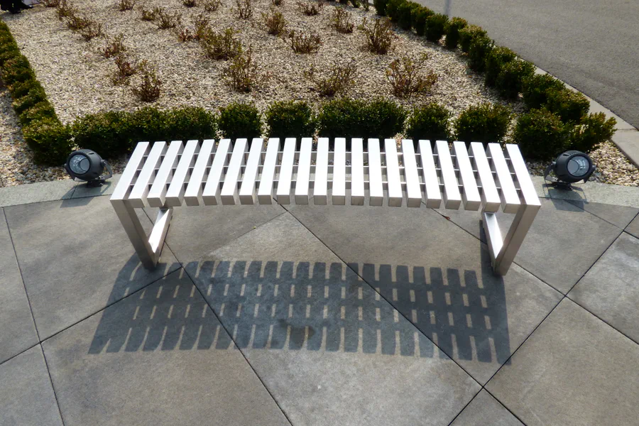 Nerezová oblouková lavička na zpevněné ploše před vstupem do budovy