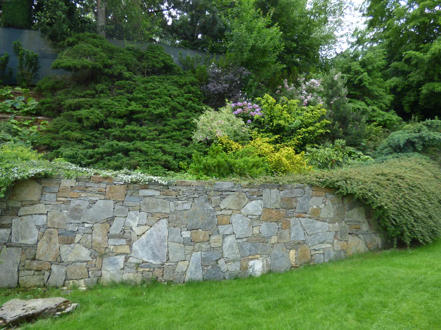 Vlnící se opěrná zídka z přesně slícovaných kamenů ve svahu zahrady