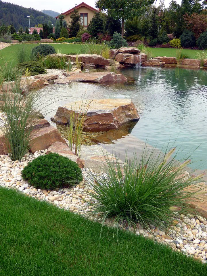 Okraj jezírka s kamenným mostem a prameništěm v pozadí